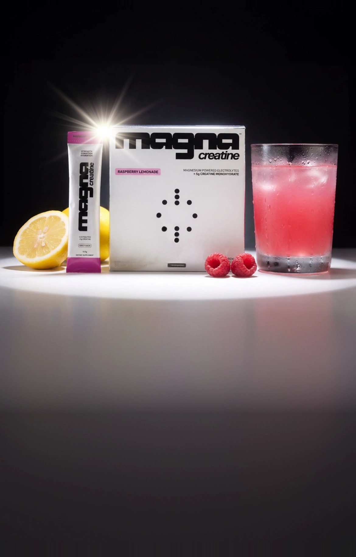 magna creatine box and stick pack with lemon, raspberries and a glass of pink drink on a dark set