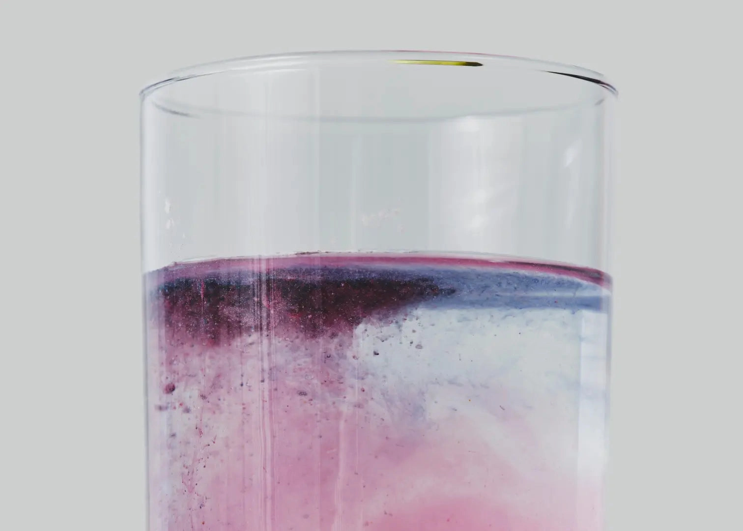 Close-up of swirling pink, blue, and purple liquid in a transparent glass.