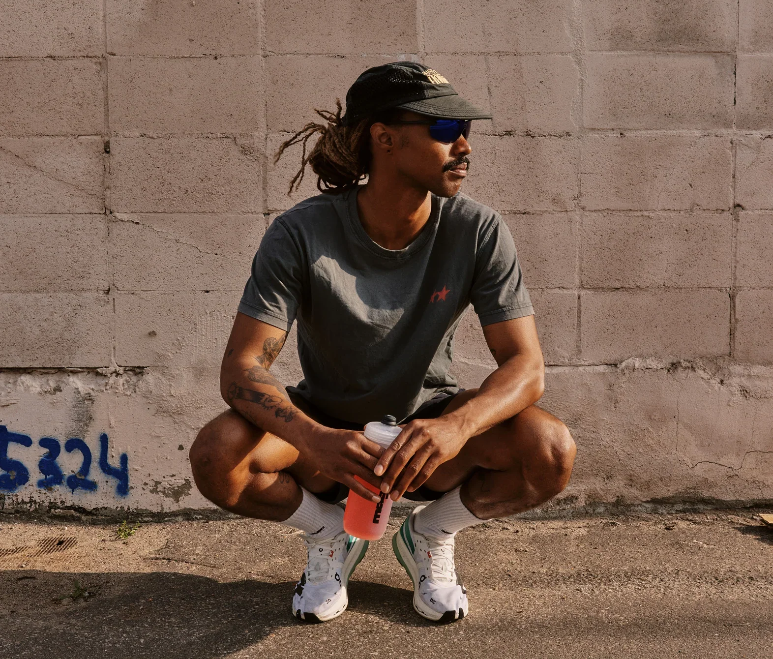 Runner crouching by a wall with a bottle of pink drink