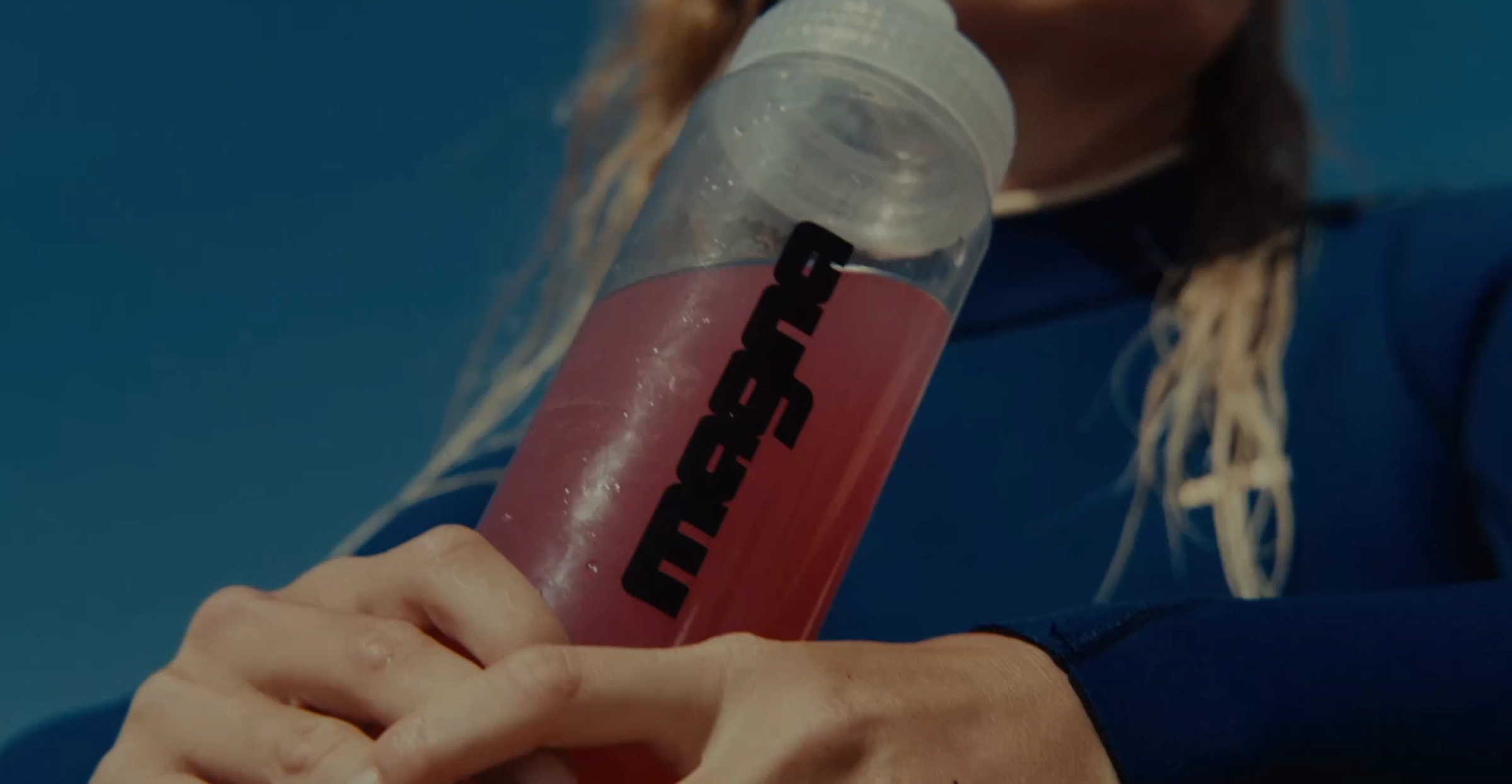 A magna bottle of pink drink being shaken, seen from below against a blue sky
